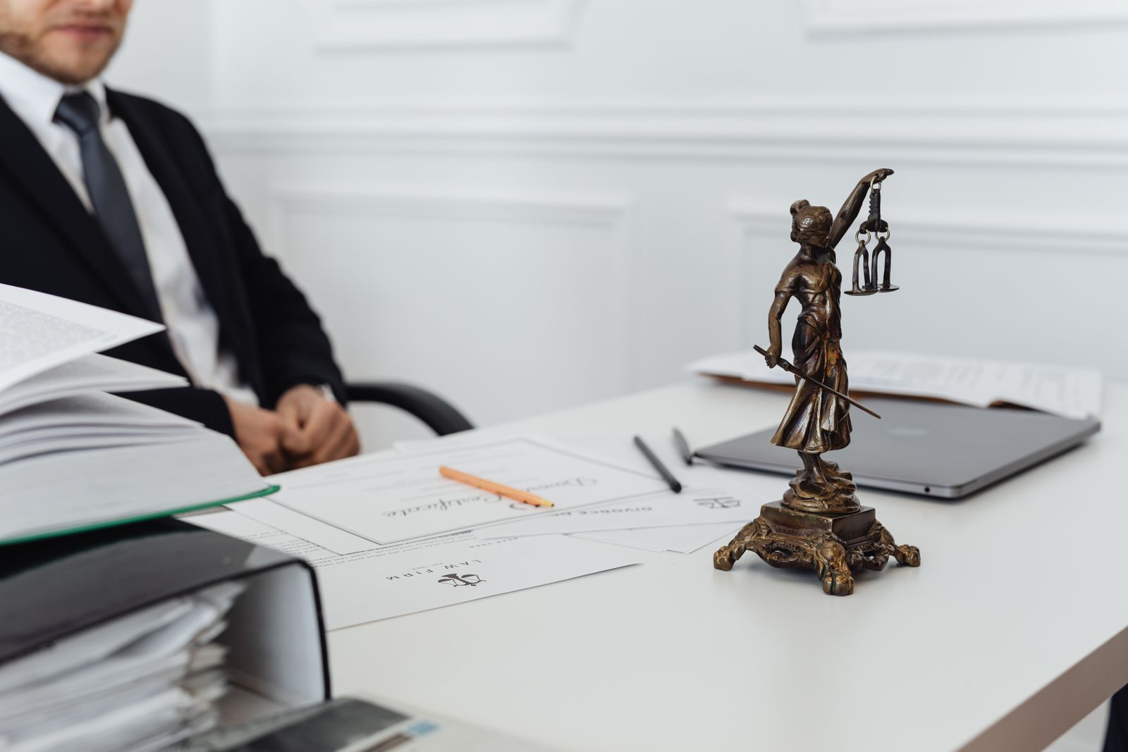 Schreibtisch einer Kanzlei mit Justitia-Figur, Unterlagen und Laptop